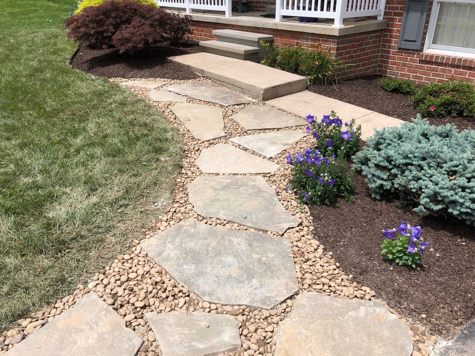 Stone walkway leading to a house, bordered by brown mulch, tan gravel, and greenery Mechanicsburg, PA.