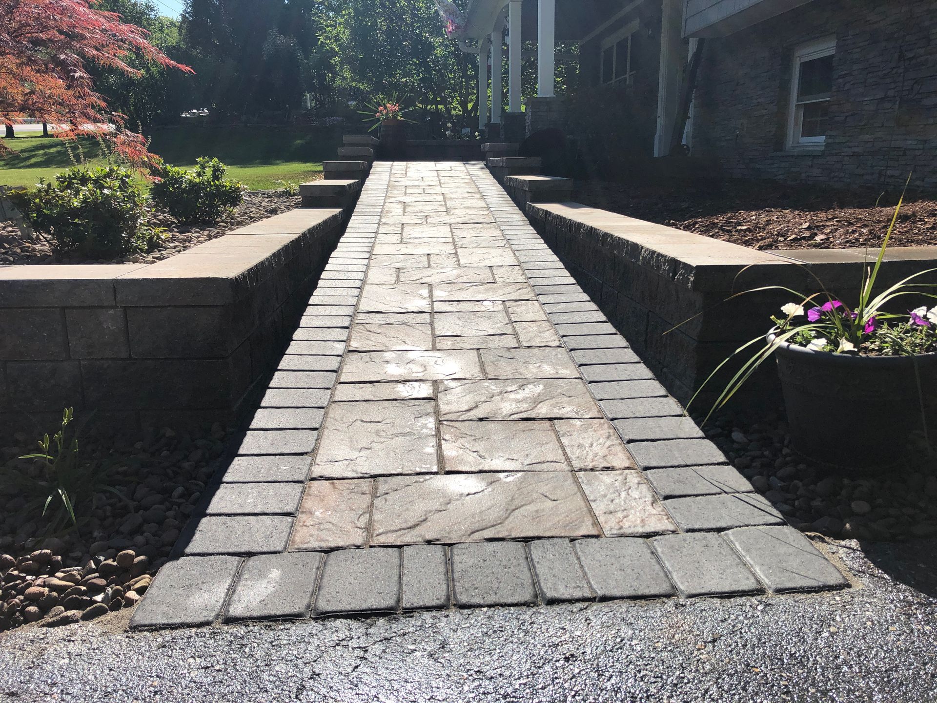 Brick walkway leading up to a house with a retaining wall and planters; gravel in the foreground Mechanicsburg, PA.
