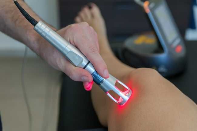 Handheld laser device treating skin on an arm, with red light glowing at the contact point