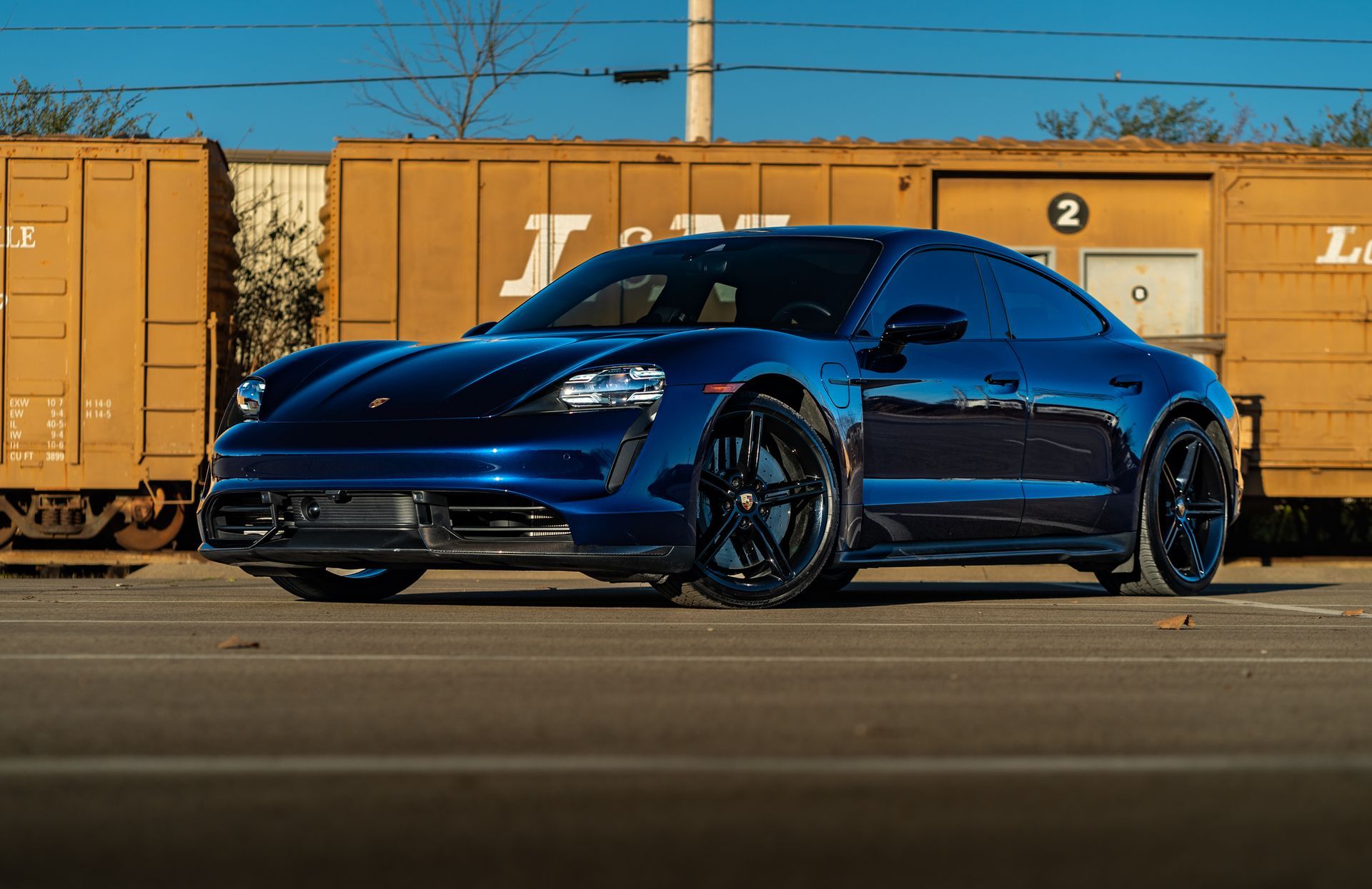 A blue porsche taycan is parked in front of a train car.