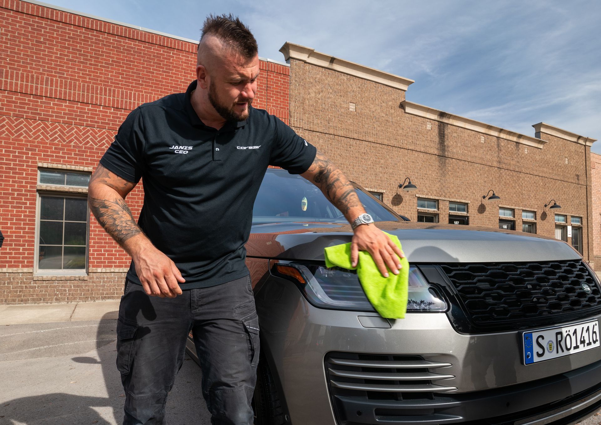 A man is cleaning a car with a towel in front of a brick building.