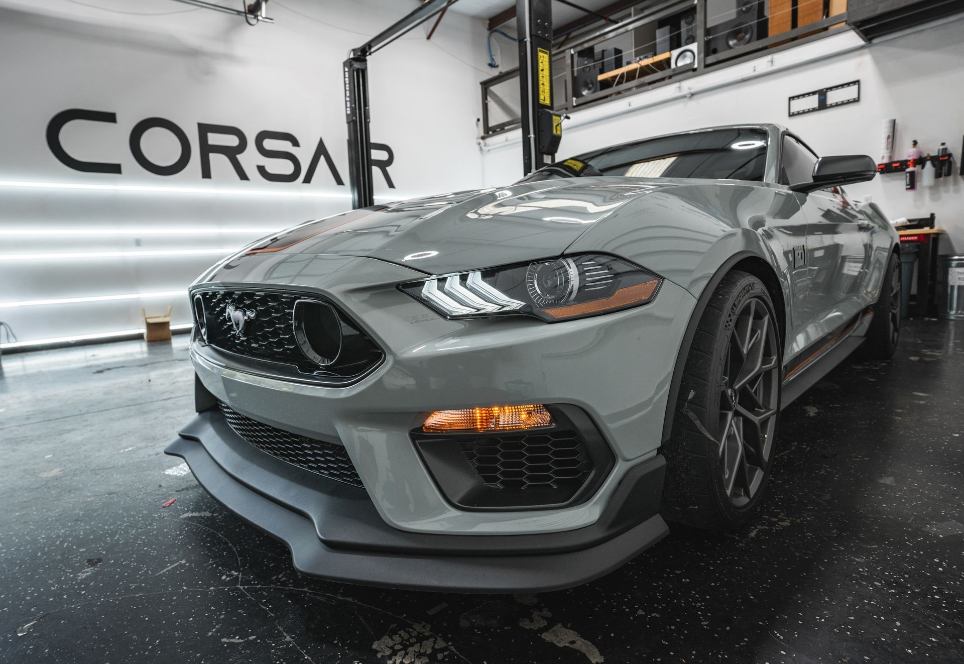 A gray mustang is parked in a garage in front of a sign that says corsar.