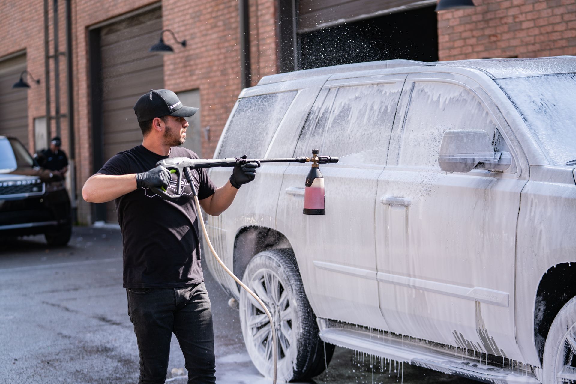 A man is washing a suv with a high pressure washer.