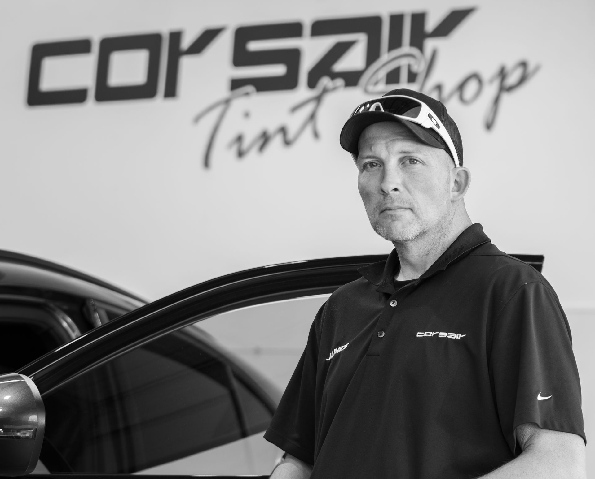A man standing in front of a car with corsair tint shop written on the wall behind him