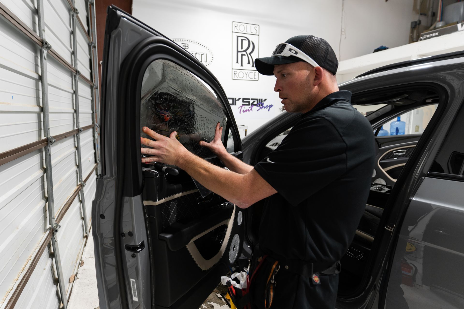 A man is installing window tinting on a car in a garage.