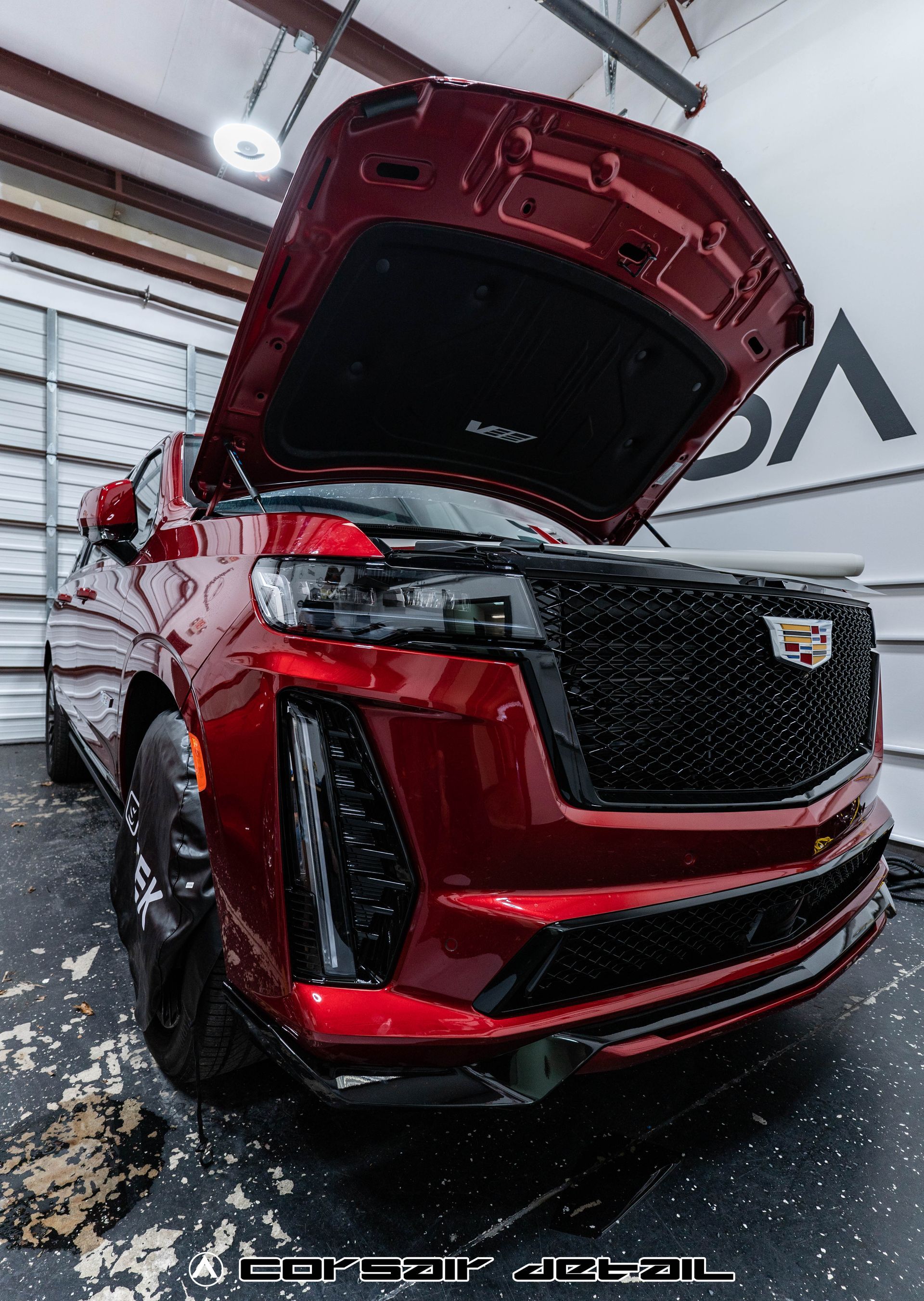 A red cadillac is parked in a garage with its hood open.