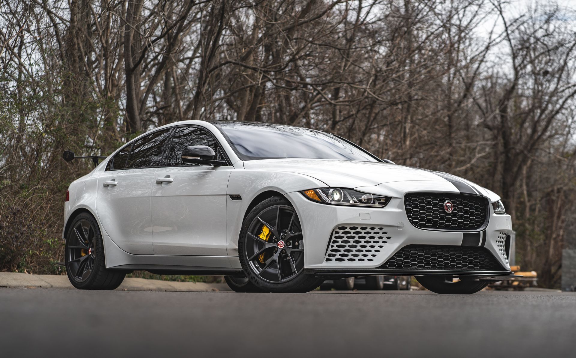 A white jaguar x type is parked on the side of the road.