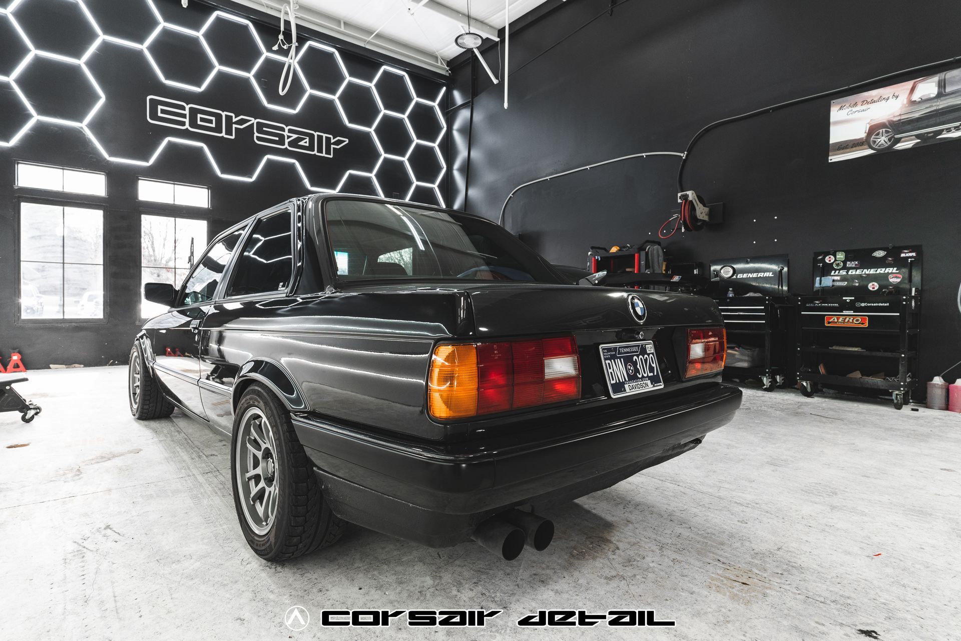 A black car is parked in a garage with a honeycomb wall behind it