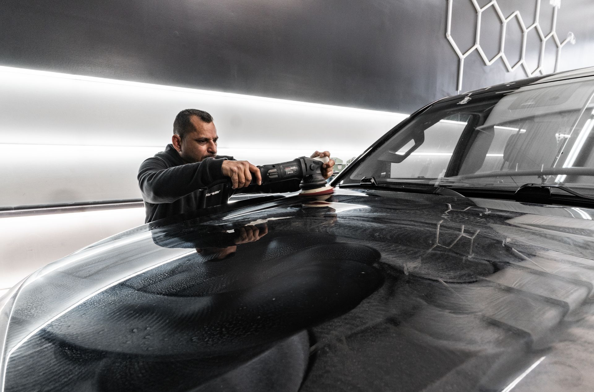 A man is polishing the hood of a black car.