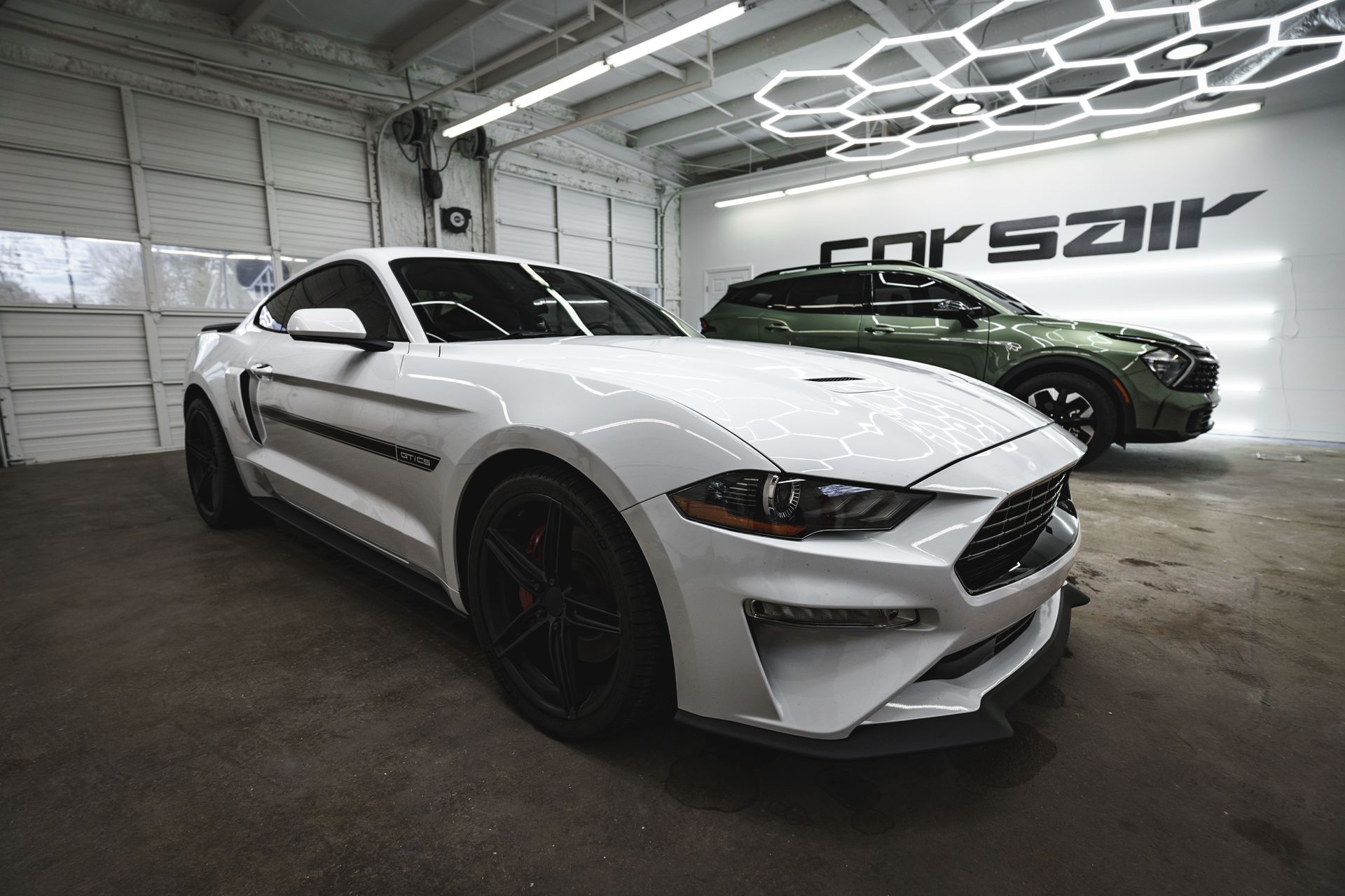A white mustang is parked in a garage next to a green suv.