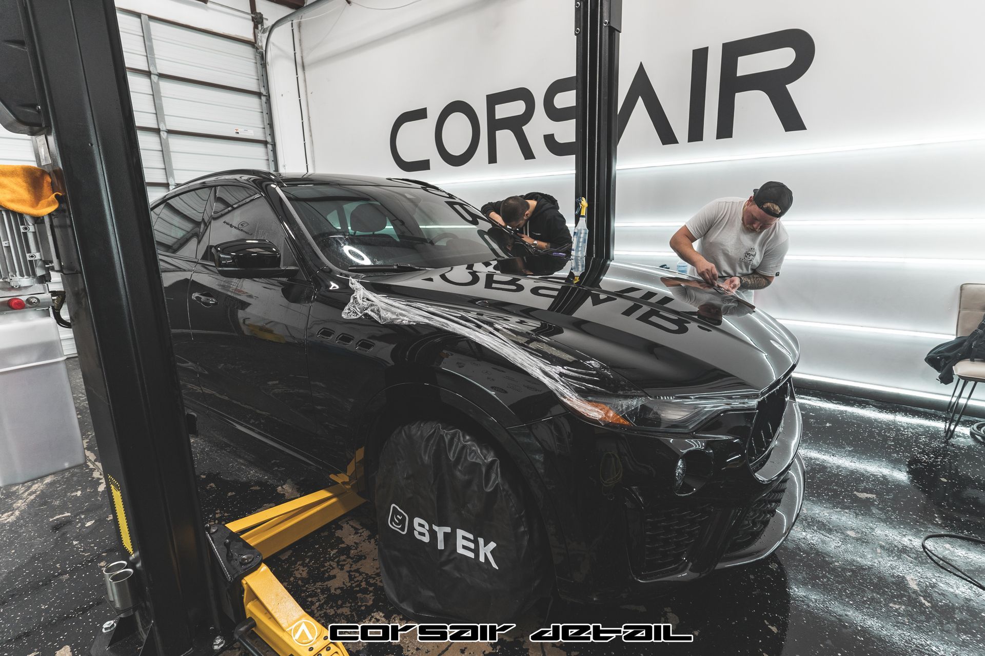 A black car is sitting on a lift in front of a wall that says corsair