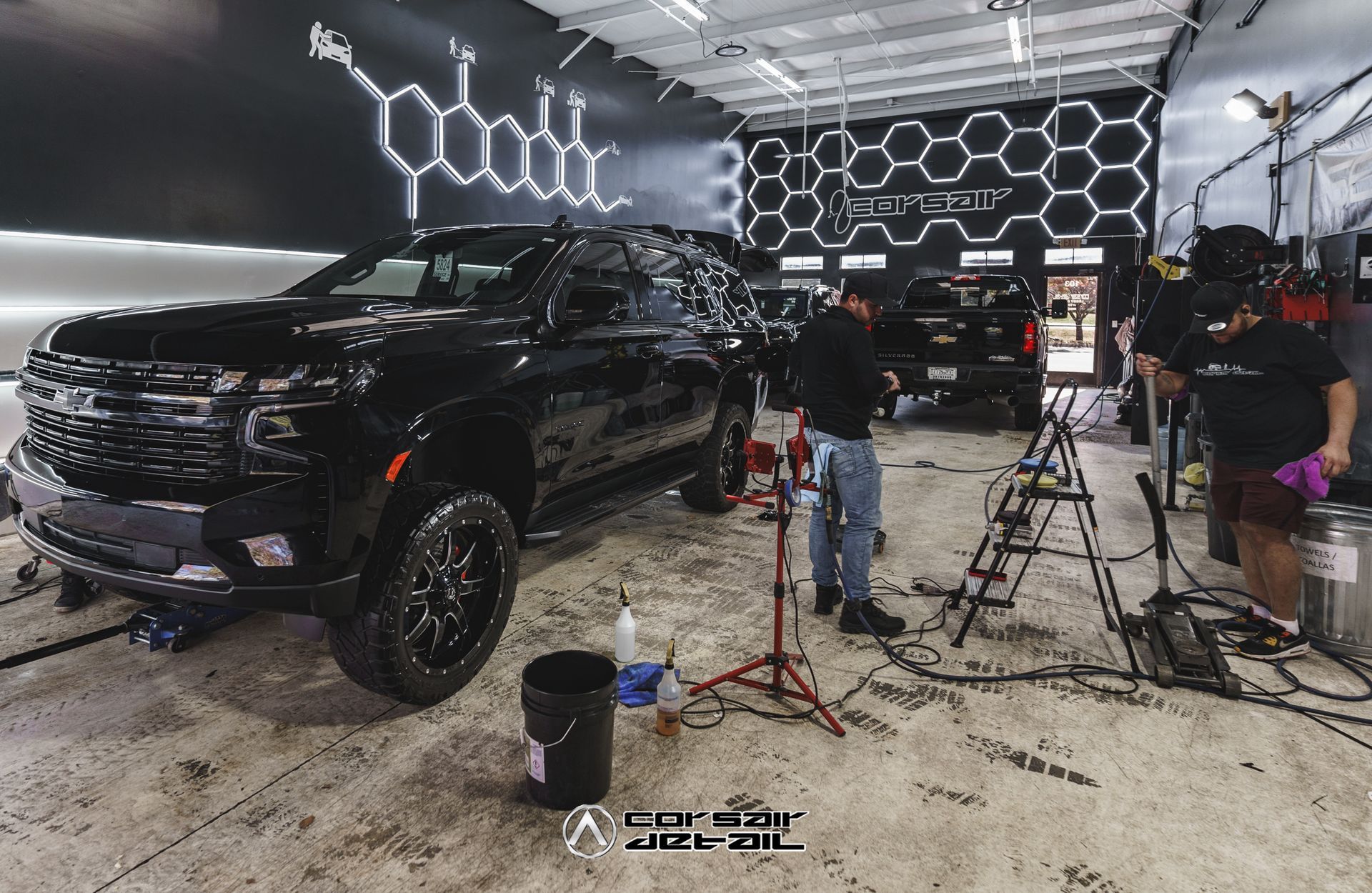 A black truck is parked in a garage with people working on it.