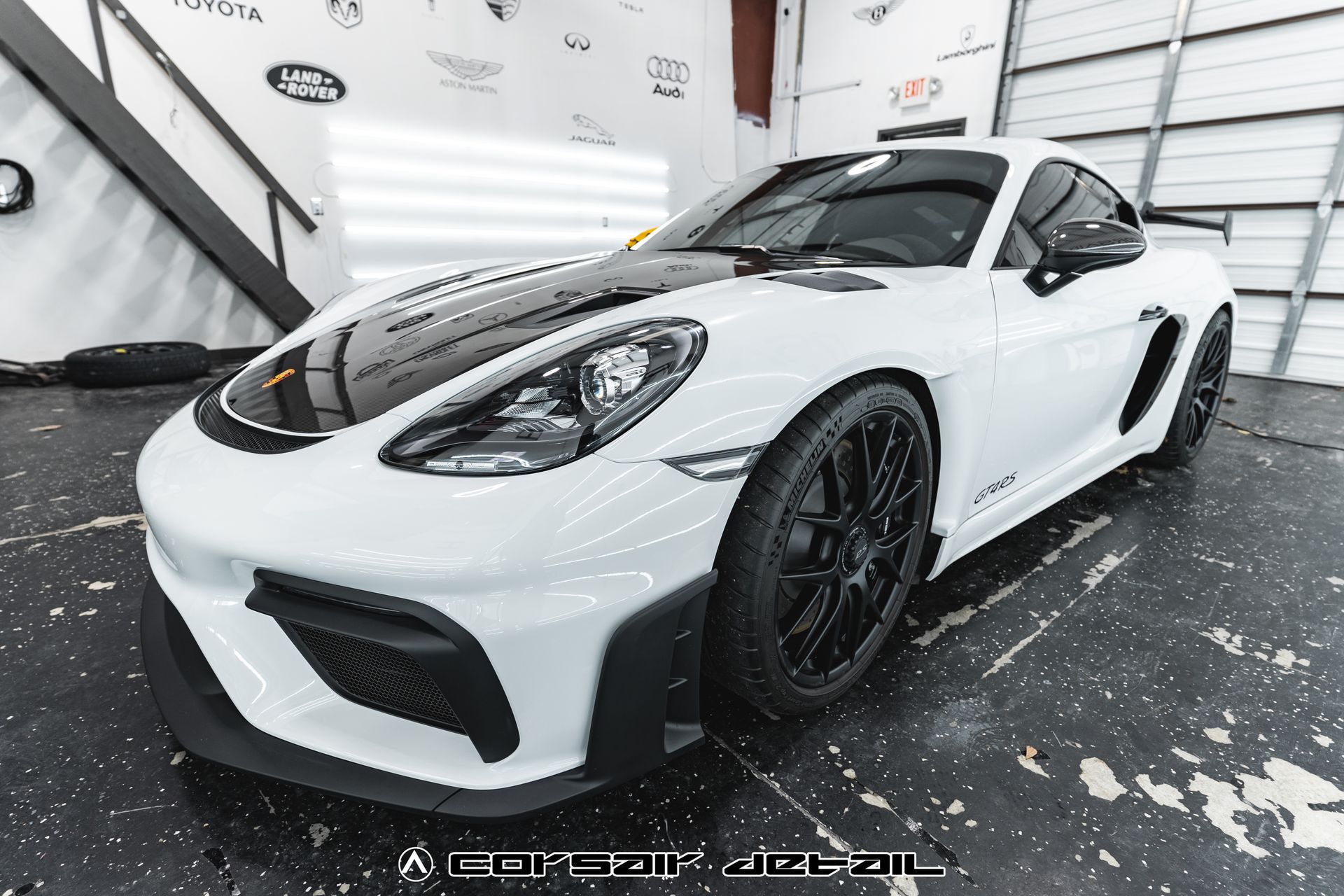 A white sports car with black wheels is parked in a garage.
