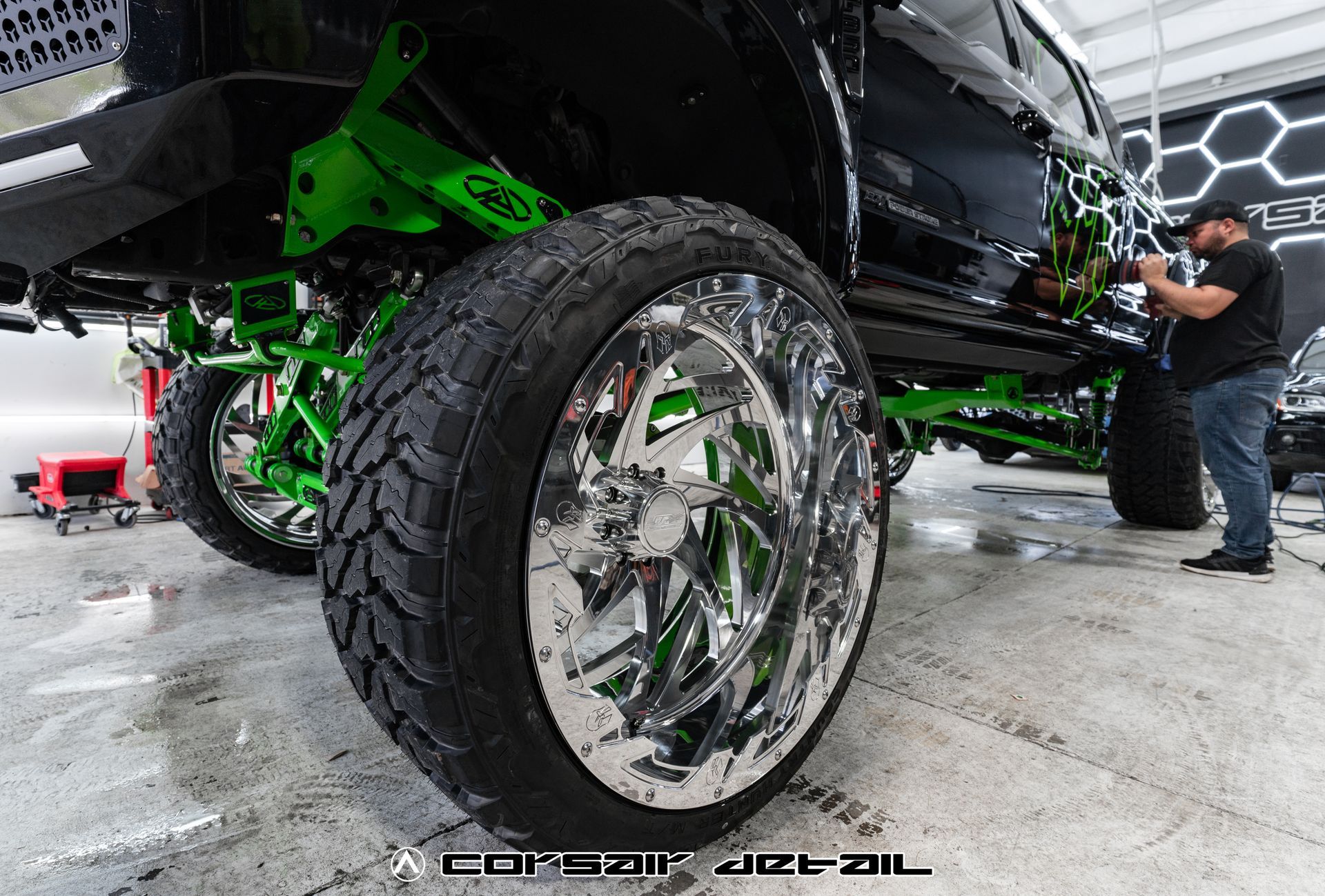 A man is working on a truck with green wheels and tires.