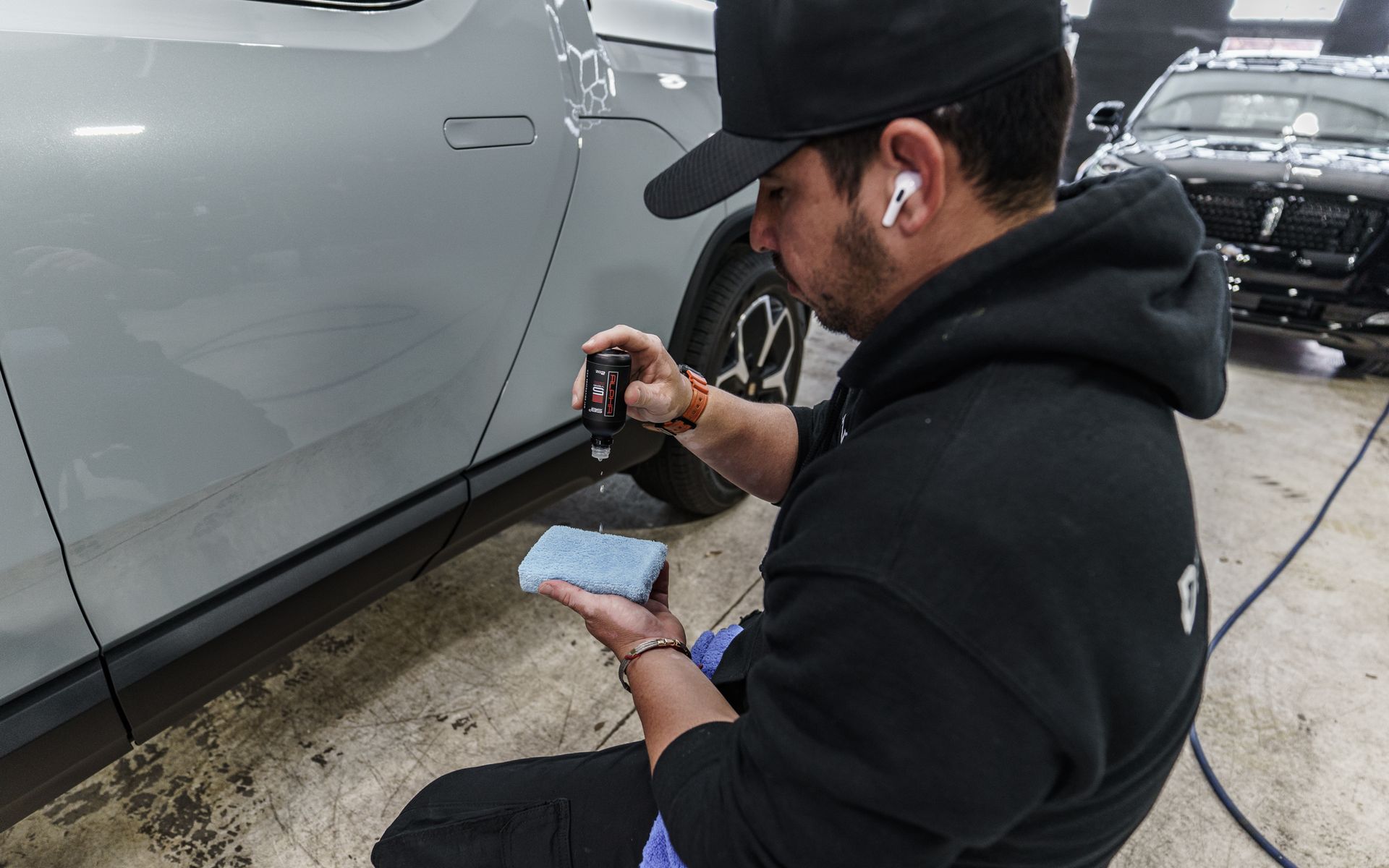 A man is kneeling down in front of a car holding a sponge.