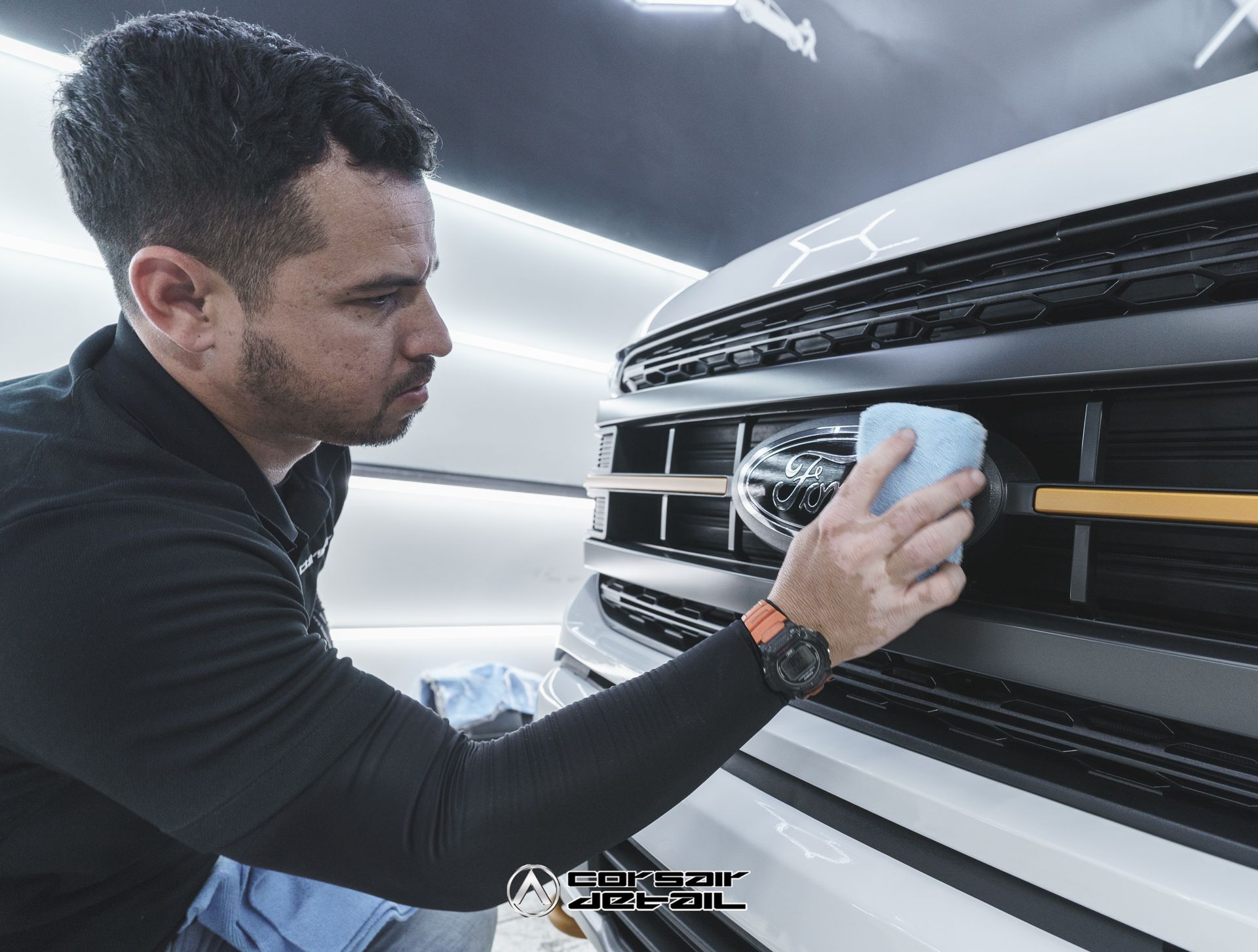A man is cleaning the front of a white truck with a sponge.