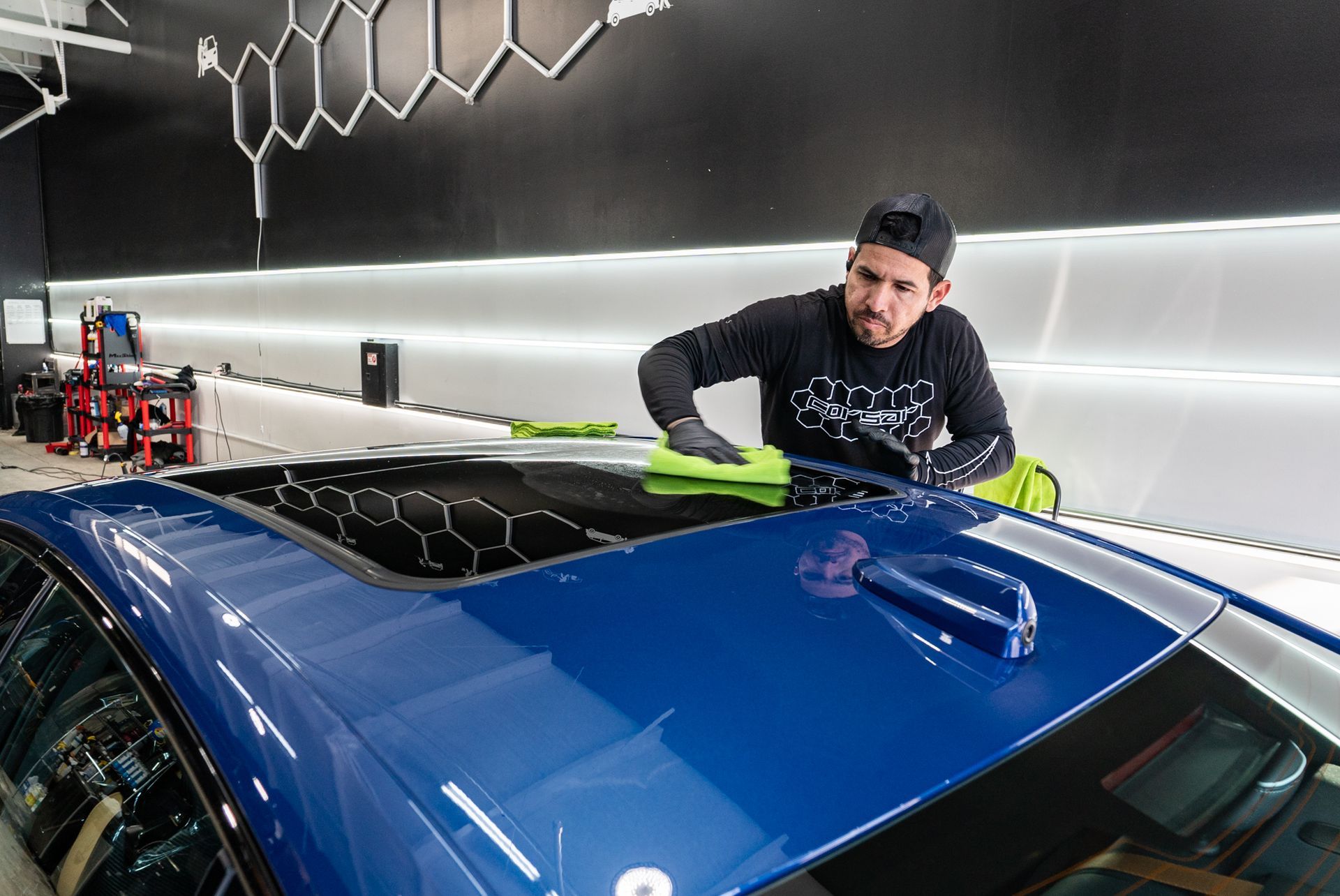 A man is cleaning the roof of a blue car.