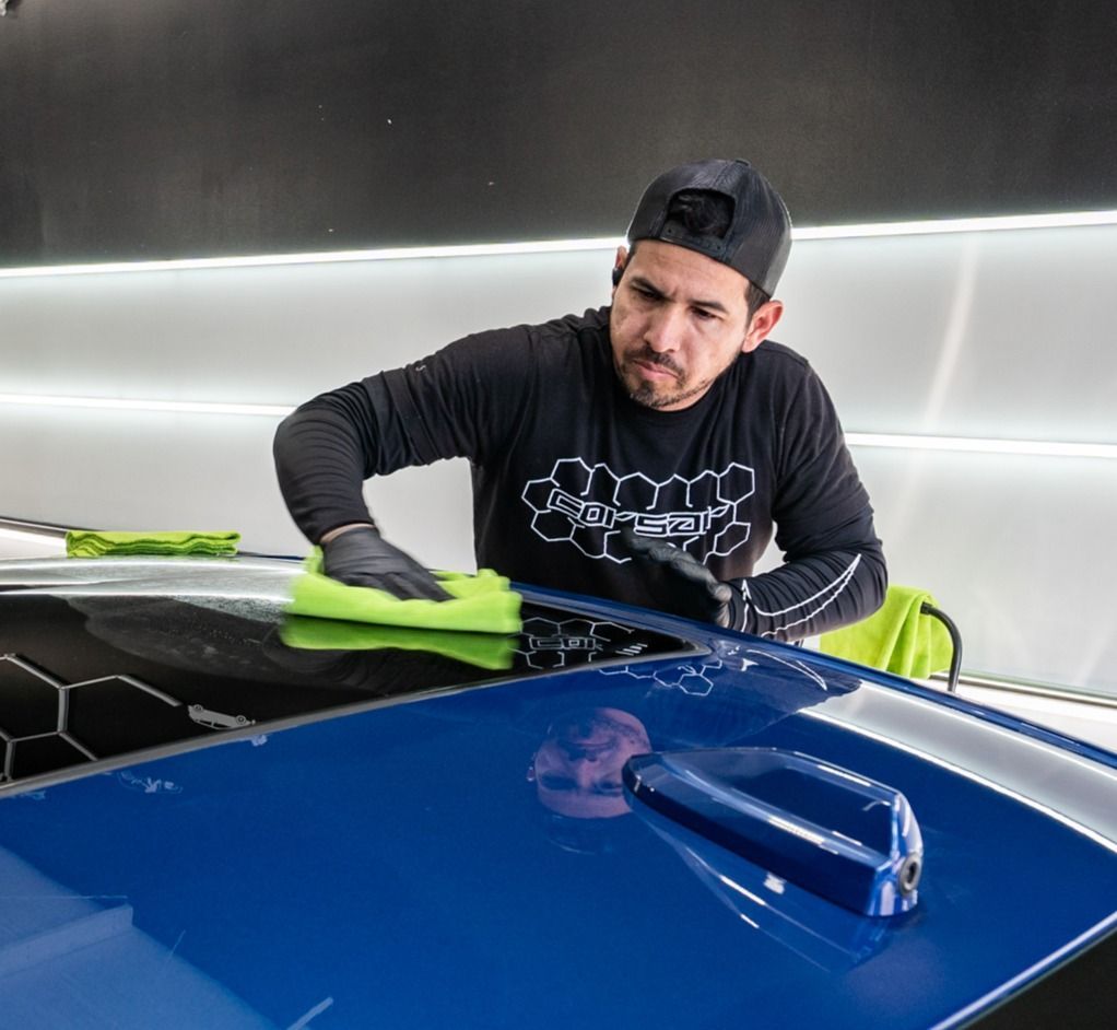 A man is cleaning the hood of a blue car with a cloth.