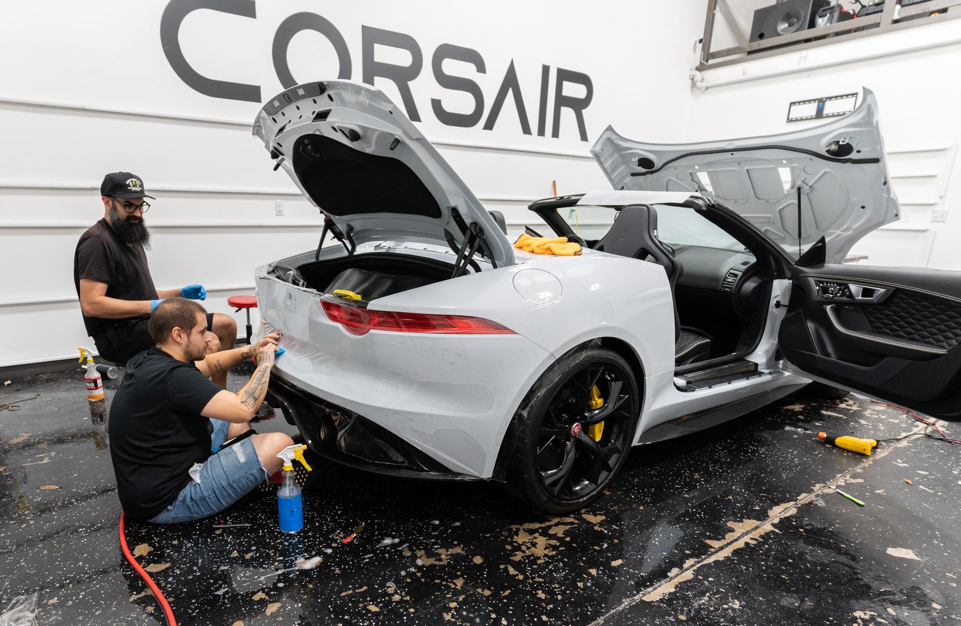 Two men are sitting on the ground working on a white sports car.