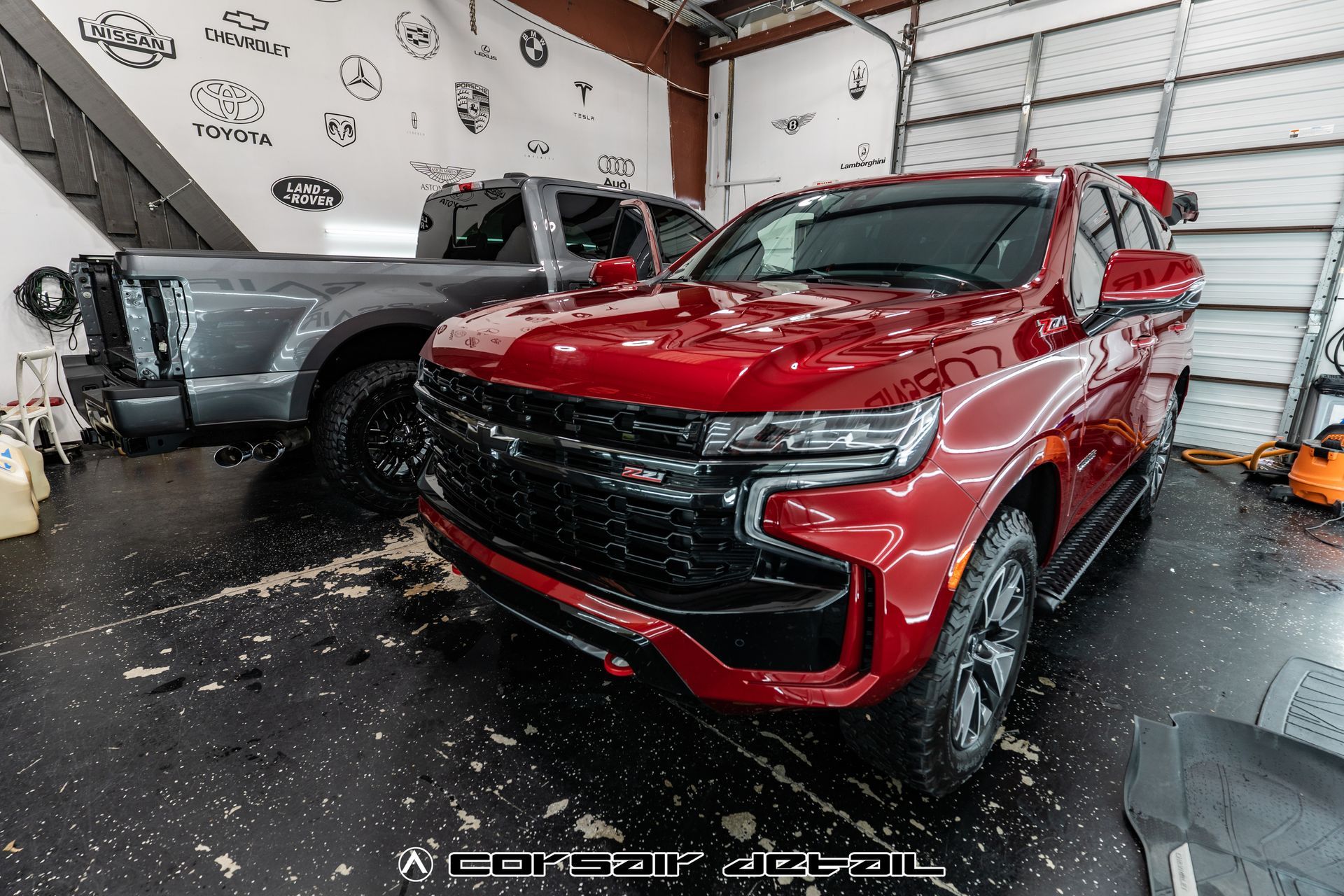 A red suv is parked in a garage next to a gray truck.