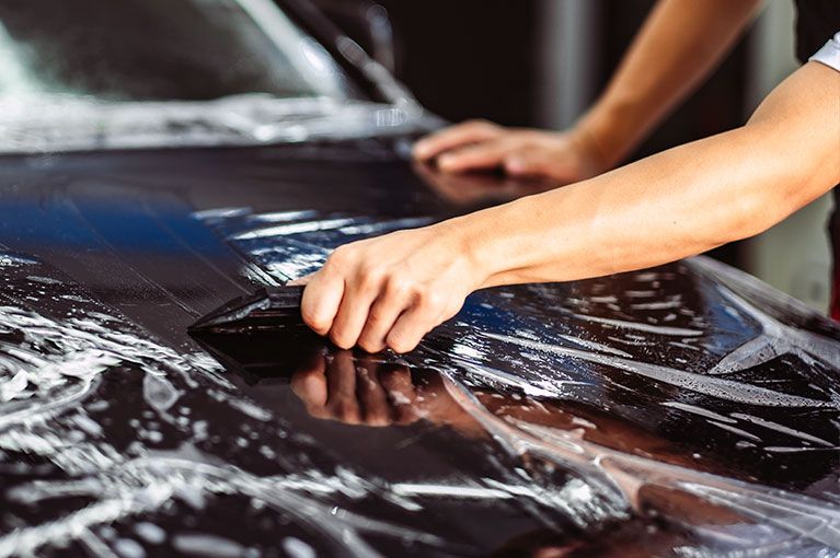 A person is applying a protective film to the hood of a car.