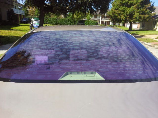 A car with a purple tinted windshield is parked in a residential neighborhood