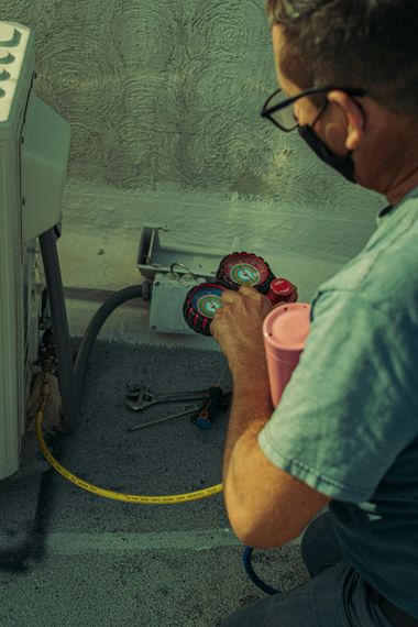 Technician connecting gauges to an HVAC unit in a workshop, with a hose and pink cup nearby