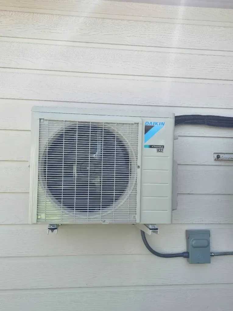 Outdoor Daikin air conditioner mounted on a white wall, with electrical box and conduit.