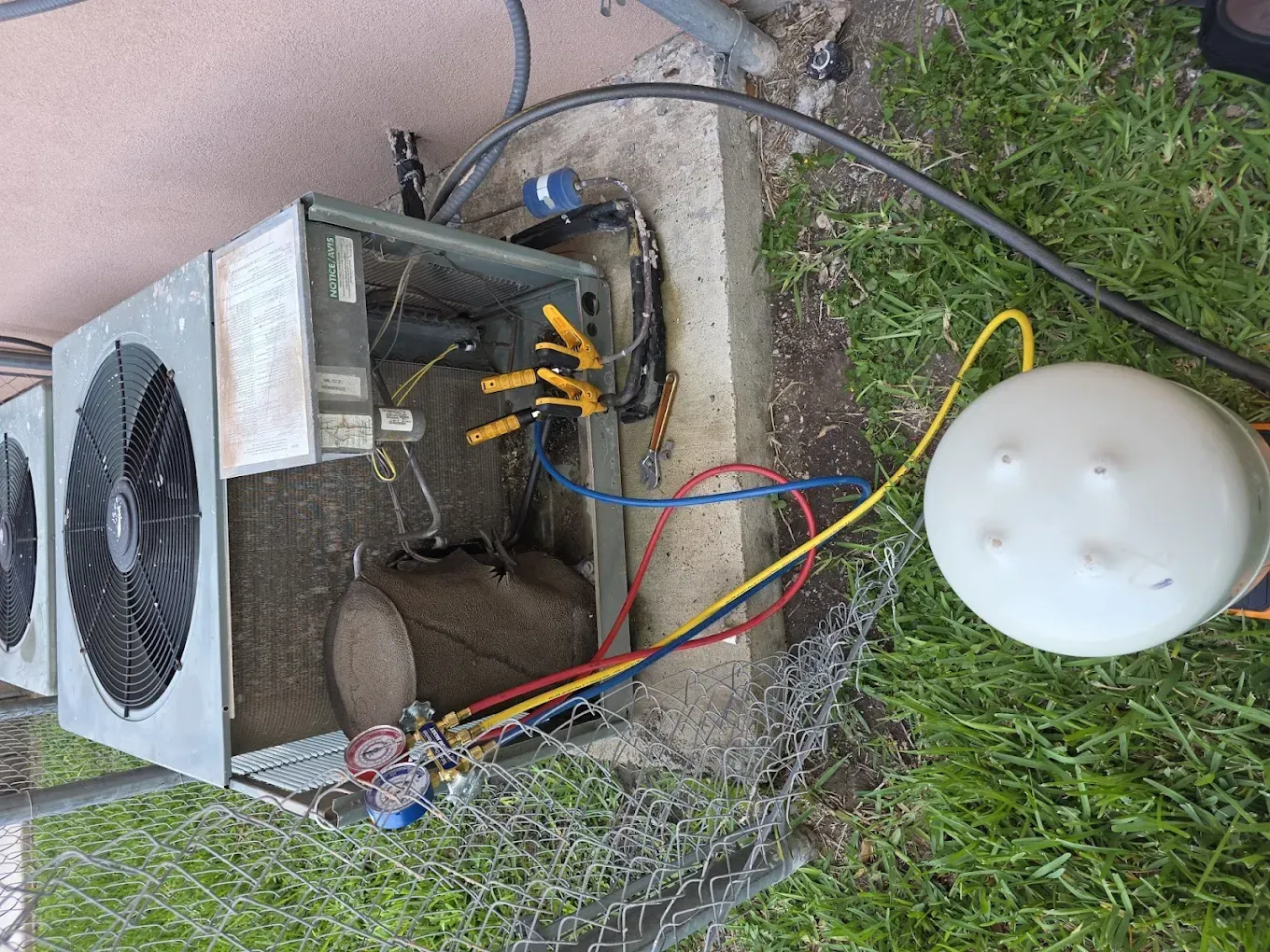 HVAC unit being serviced. Gauges and hoses connected to the unit outdoors, grassy area.