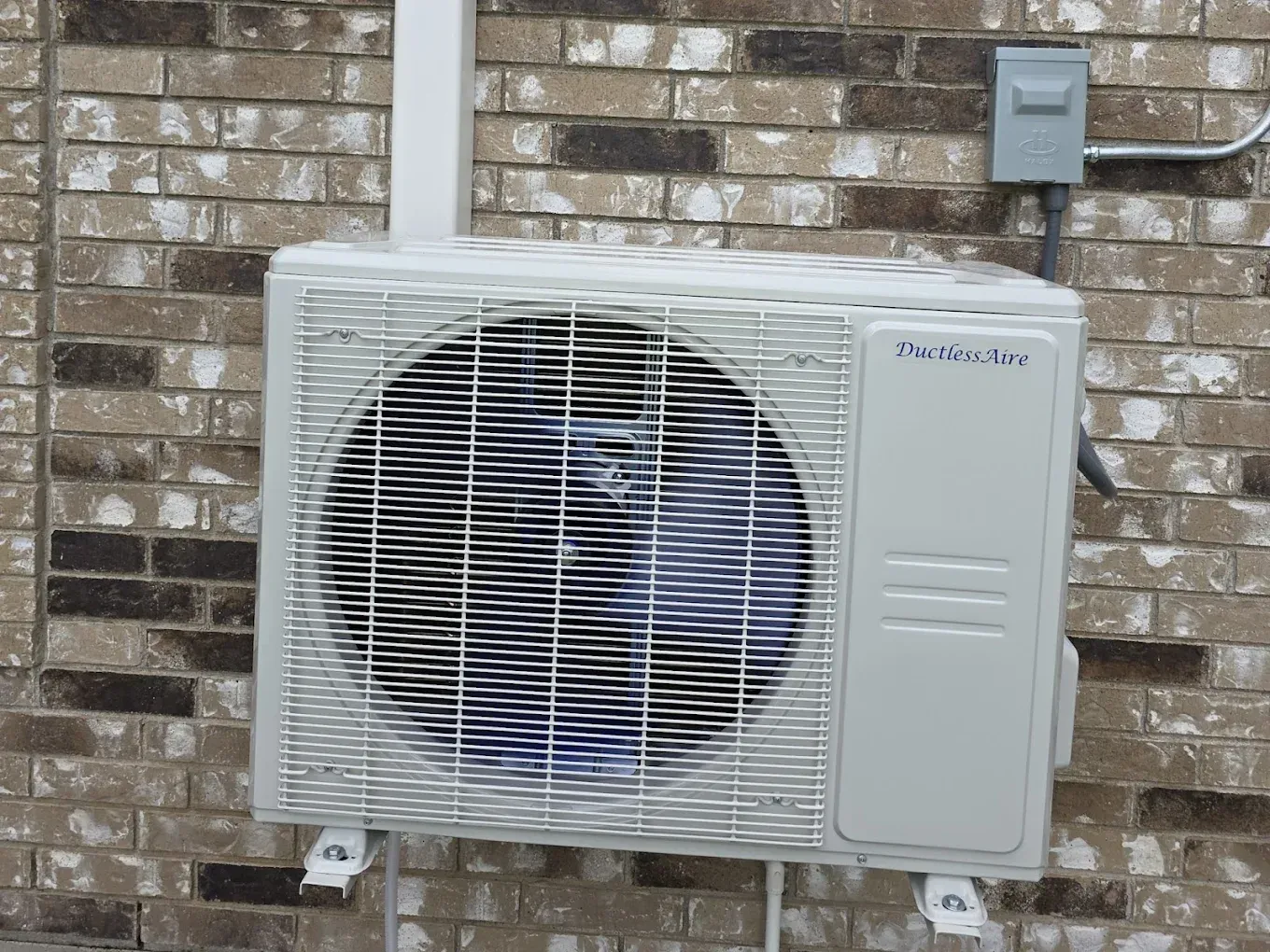 White mini-split air conditioner mounted on a brick wall with an electrical box above it.