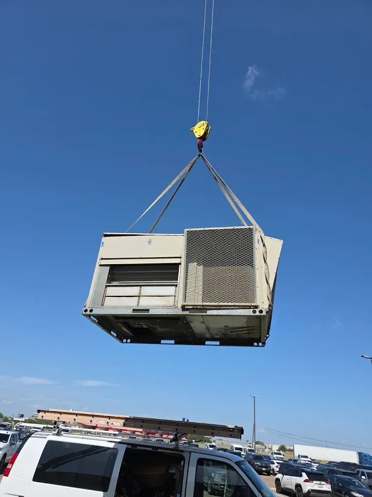 Crane lifting a large, rectangular HVAC unit against a clear, blue sky.