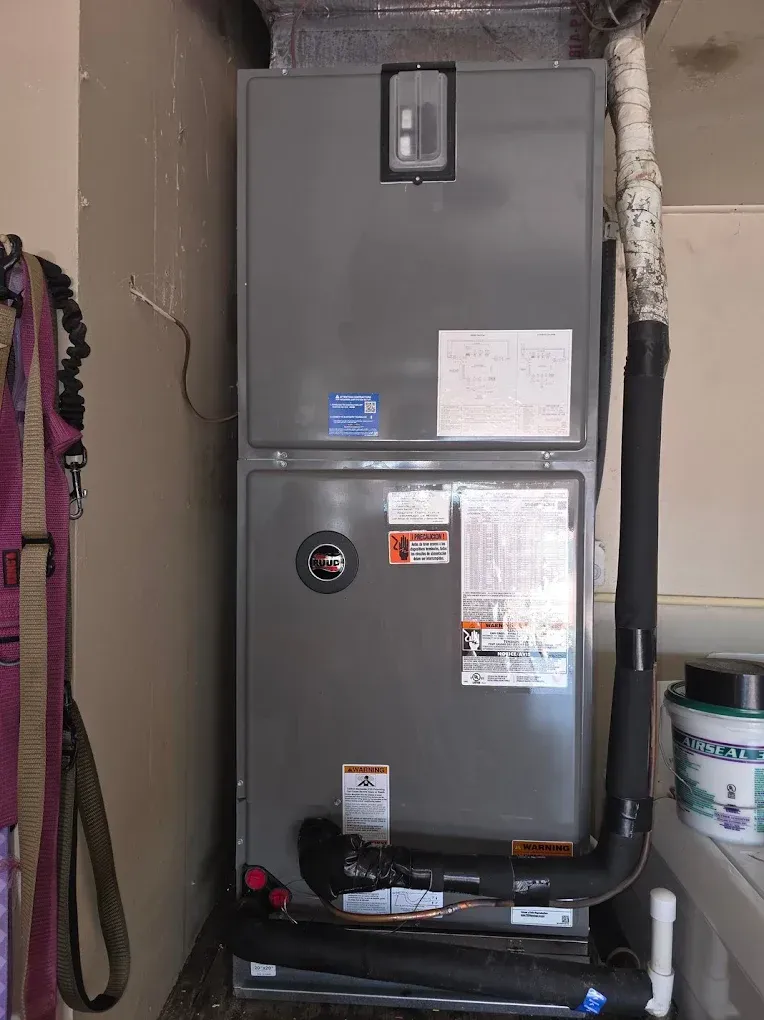 Gray HVAC unit with black insulated pipes in a utility room.