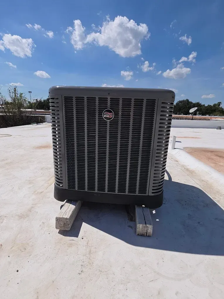 Air conditioning unit on a flat white roof with a blue sky and clouds in the background.