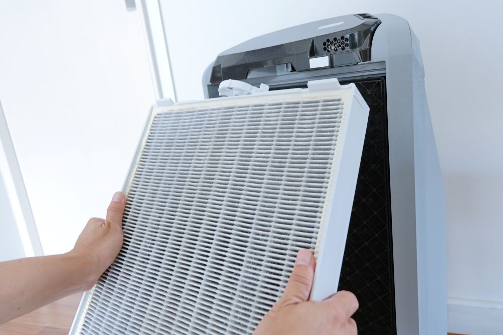 Person replacing the air filter in a gray air purifier.