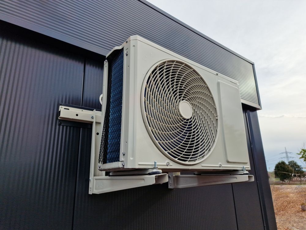 Air conditioning unit mounted on a black building's exterior wall, against a sky background.