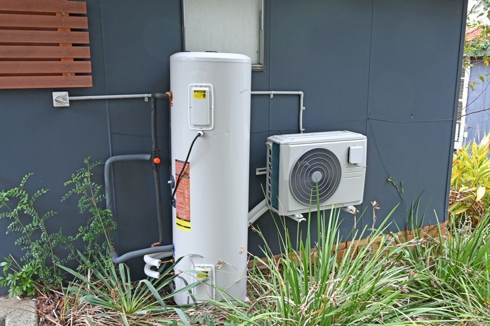 White hot water tank and air conditioner unit mounted on a dark grey exterior wall.