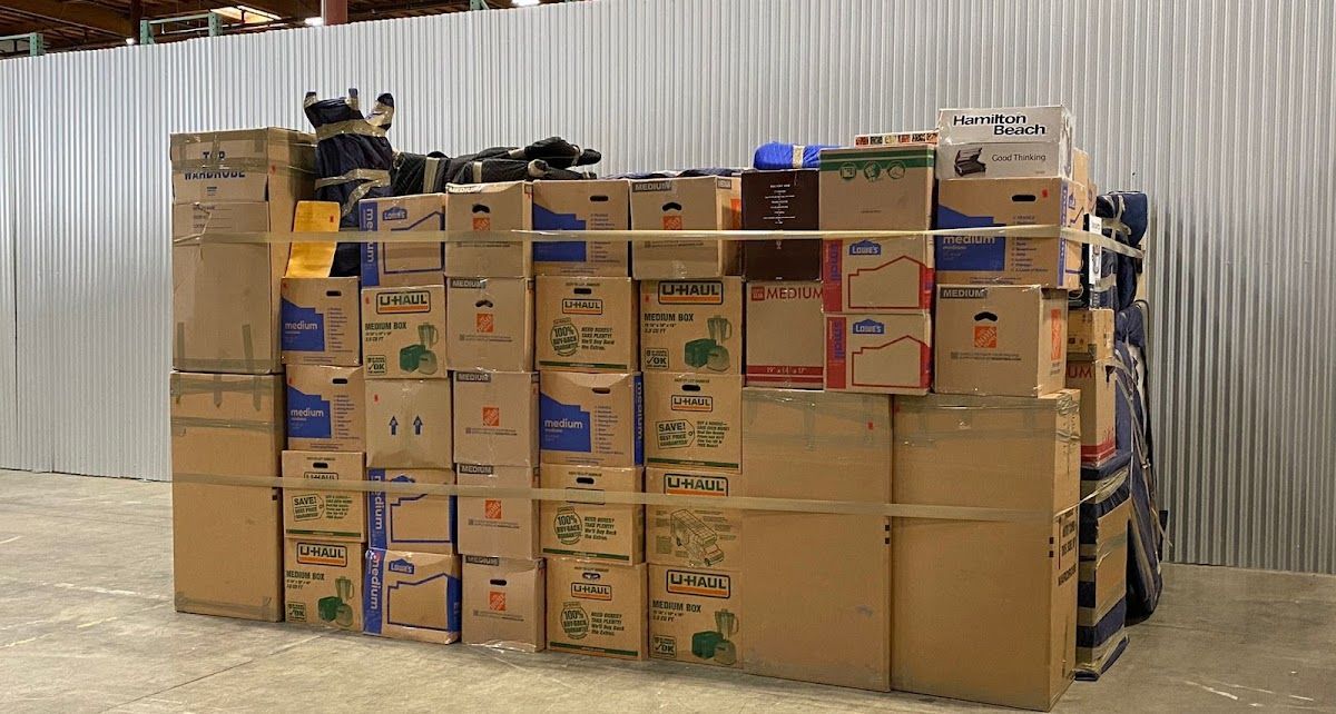 Boxes stacked high, haphazardly held together with wooden poles, against a corrugated metal wall.