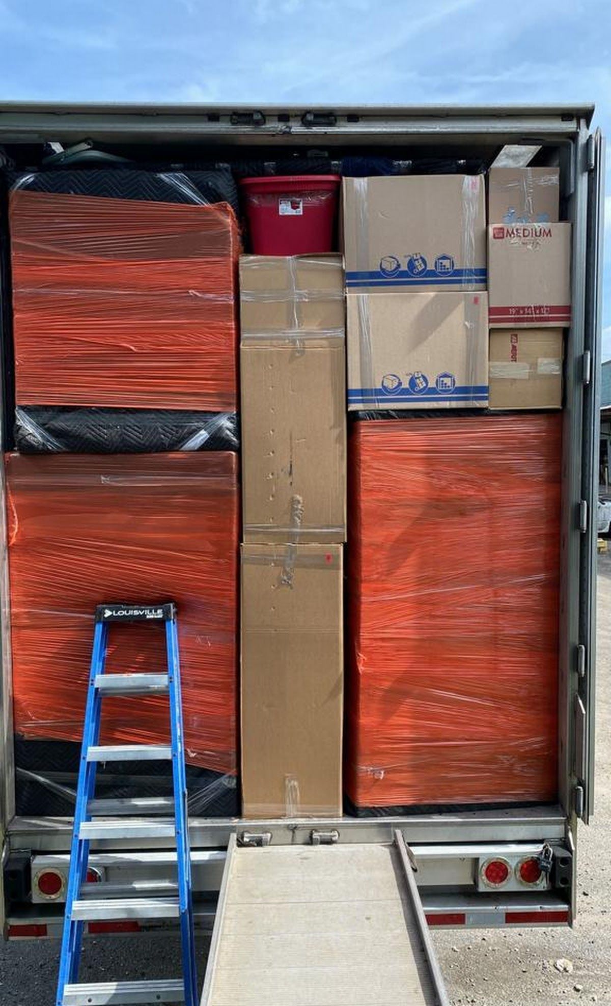 Inside of a truck filled with boxes, two large orange wrapped items and a step ladder.