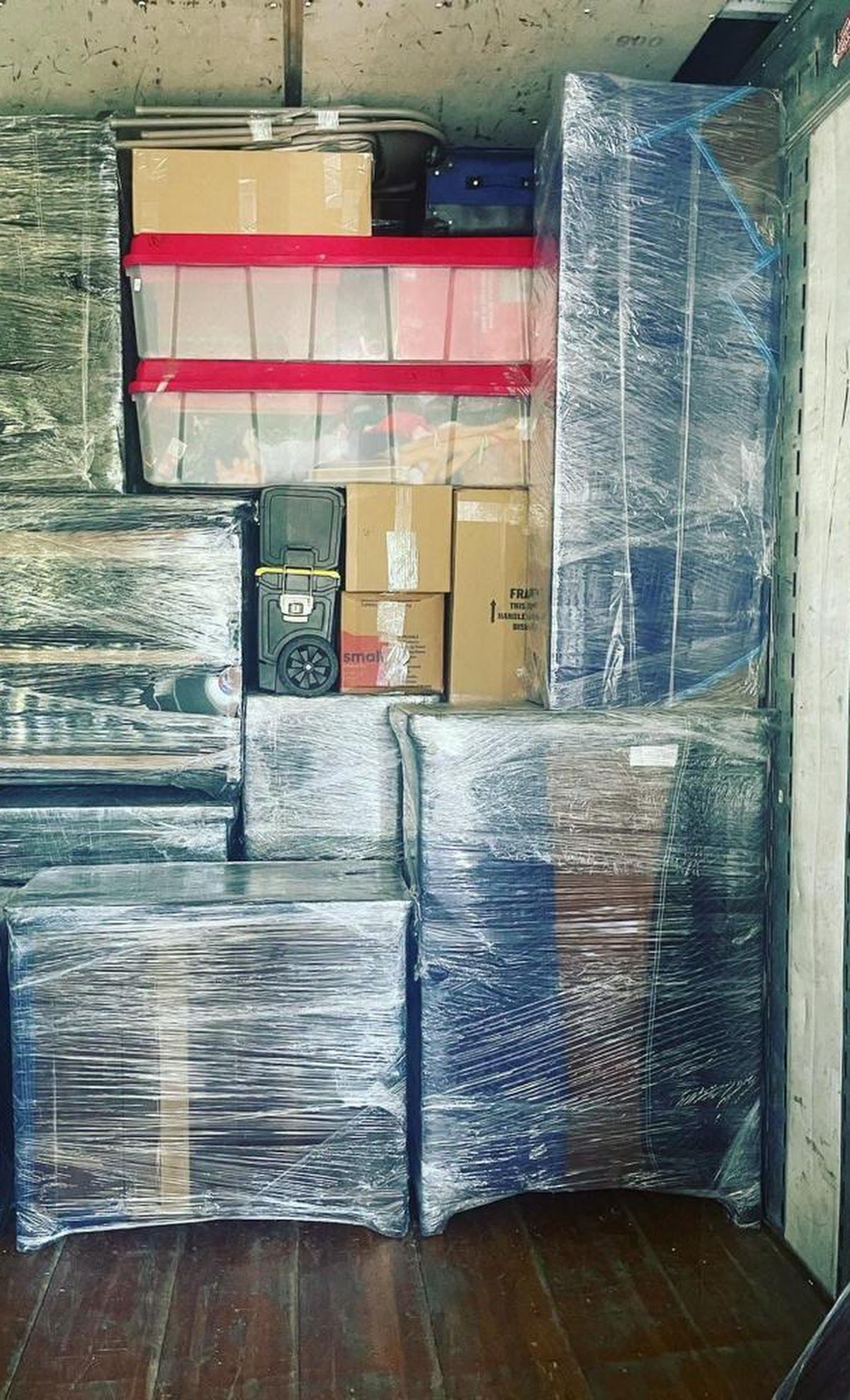 Boxes and furniture, wrapped in blue plastic, are packed tightly inside a moving truck.