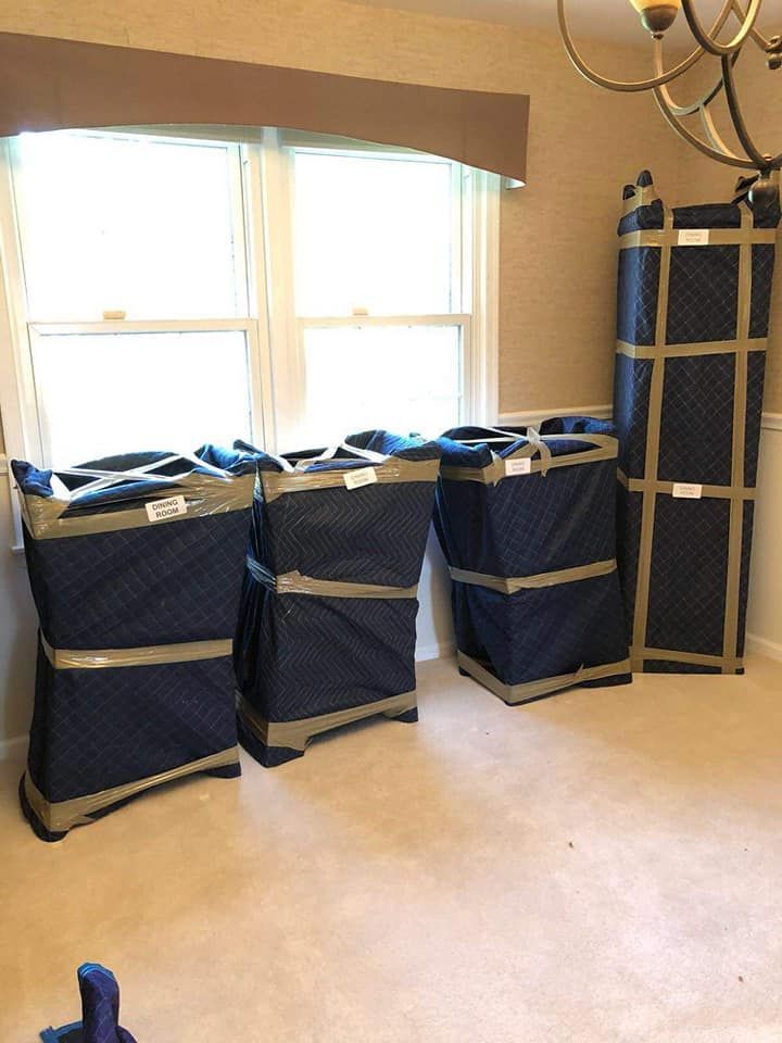 Four furniture pads in a room, stacked against a wall near a window. They are dark blue with tan tape.