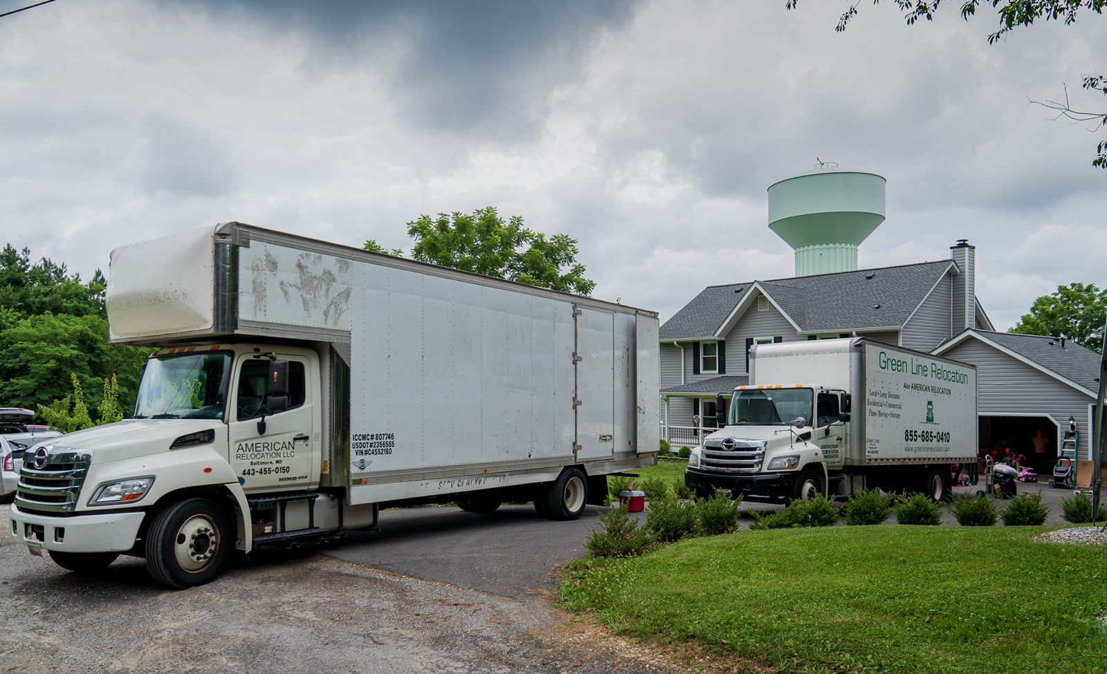 Moving trucks parked in front of a house, water tower in background.