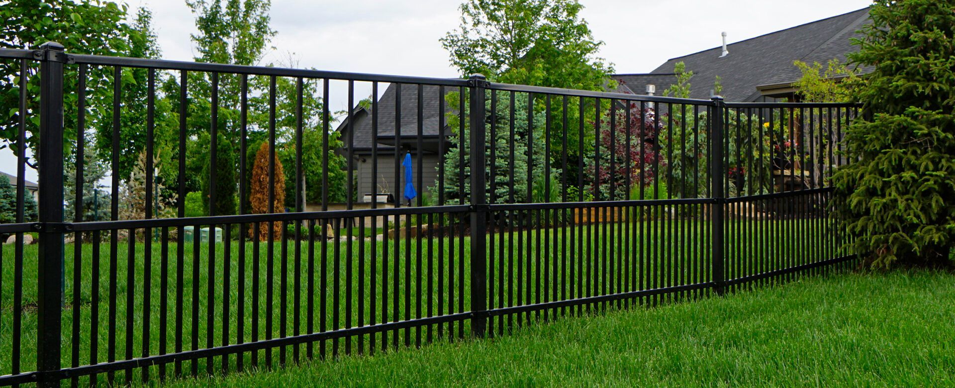 A black metal fence surrounds a lush green yard.