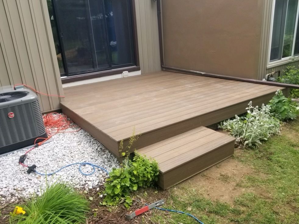 Composite deck with steps, next to house.  Features air conditioner unit, white gravel, and plants.
