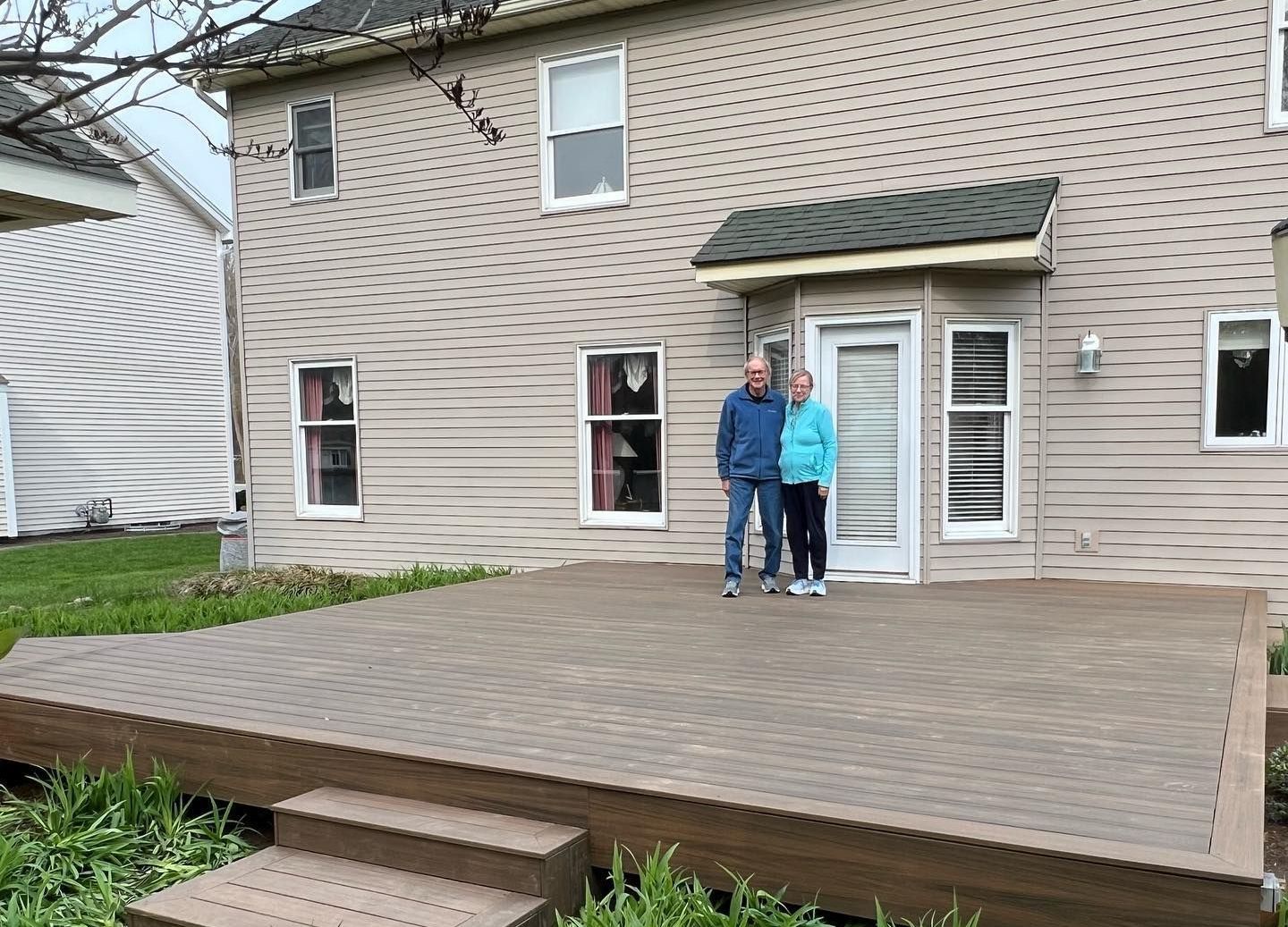 A man and a woman are standing on a deck in front of a house.