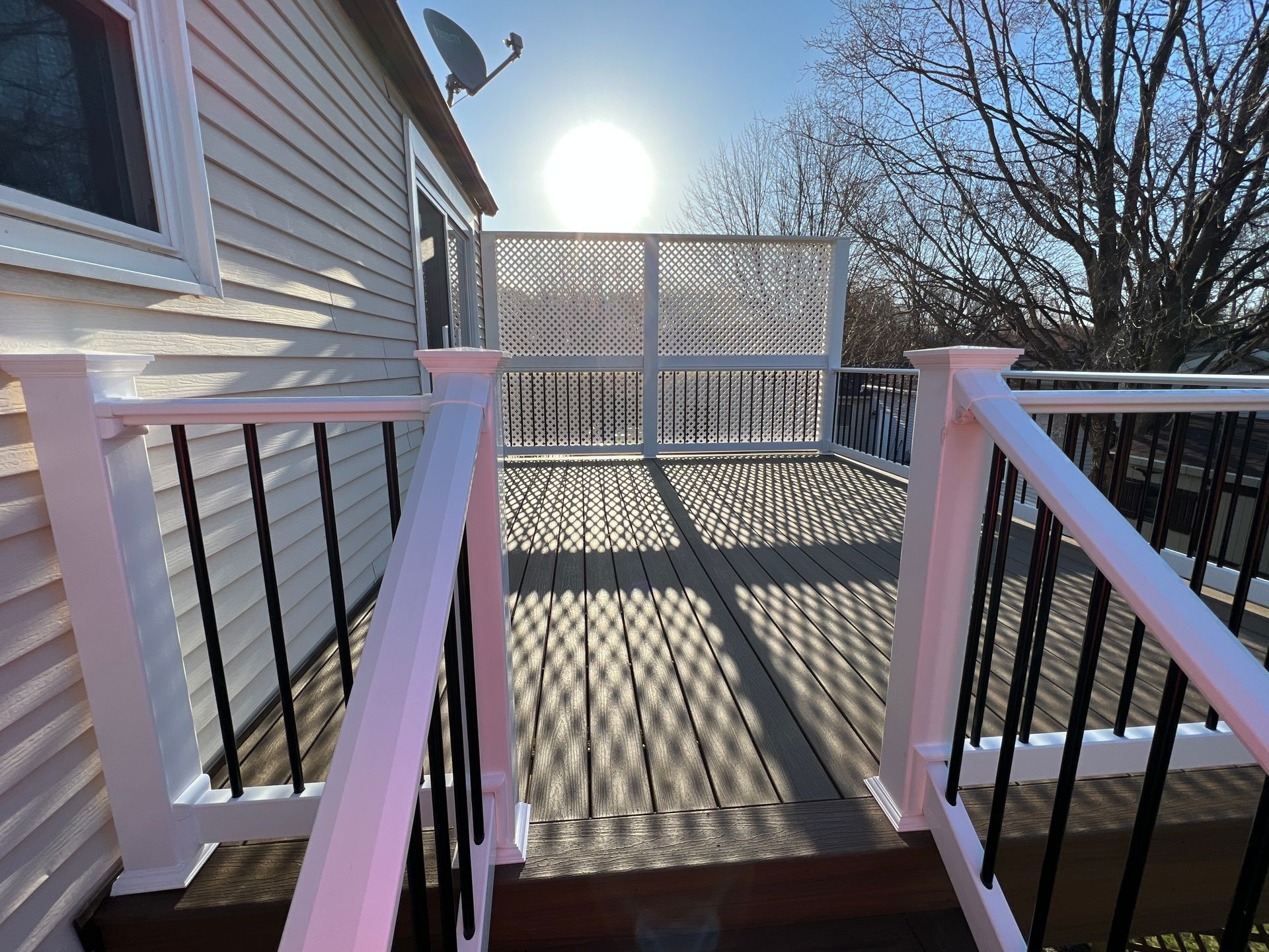 A white house with a wooden deck and stairs leading to it.