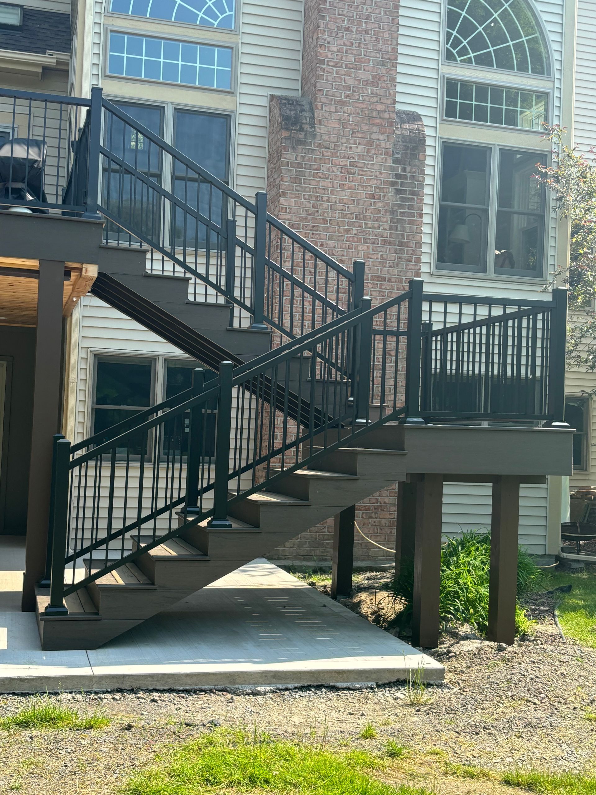 Dark brown deck with black railing and stairs leading to a house with large windows and a brick chimney.