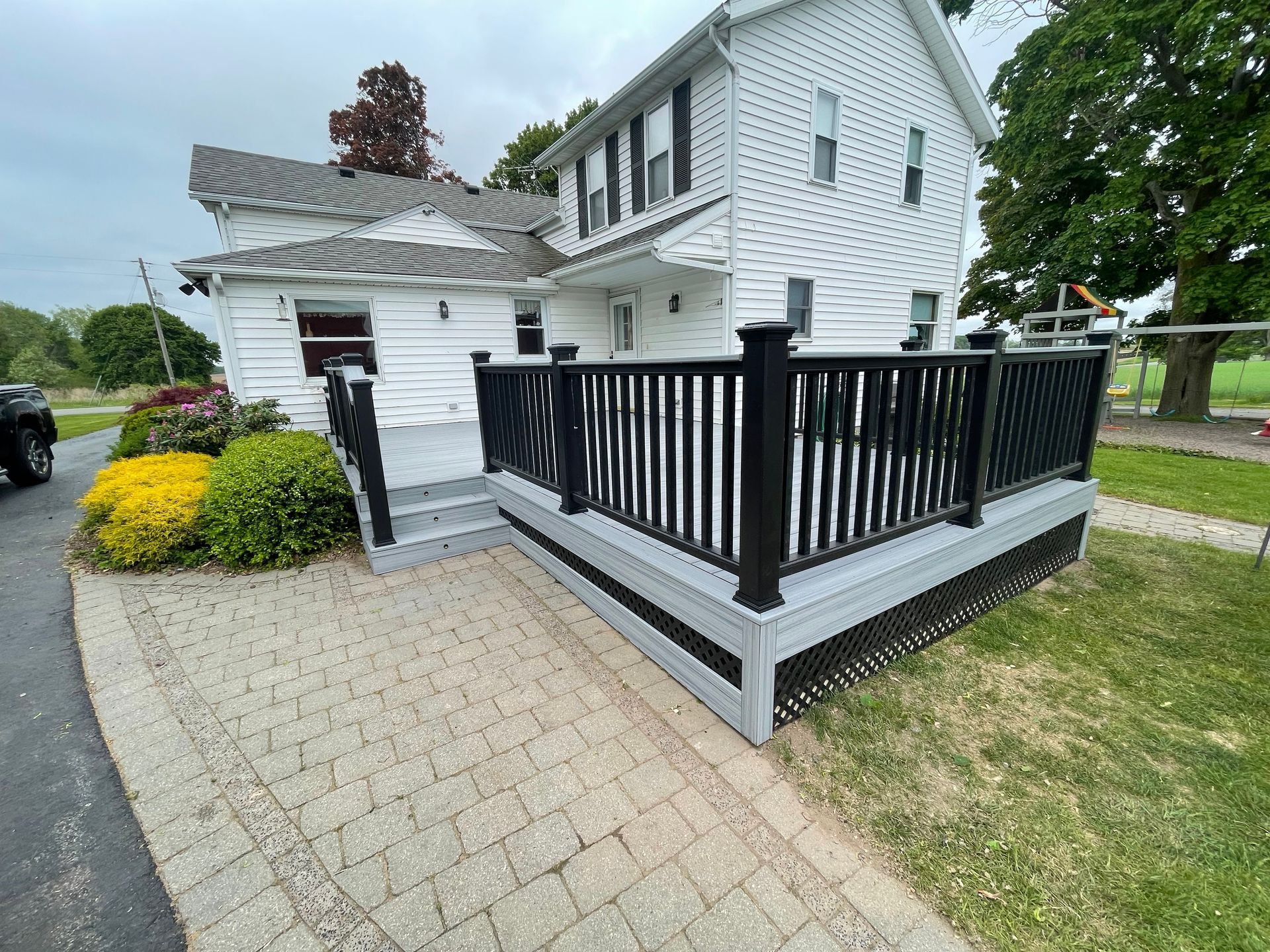 White house with black deck railing, gray decking, and a brick pathway.