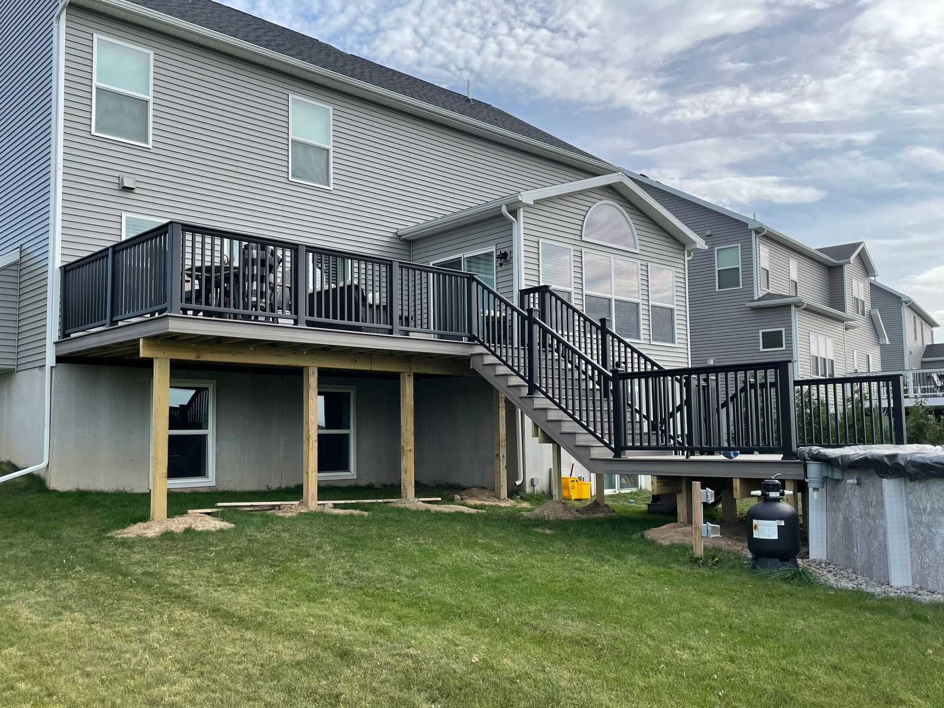 A large deck with stairs leading up to it is in the backyard of a house.