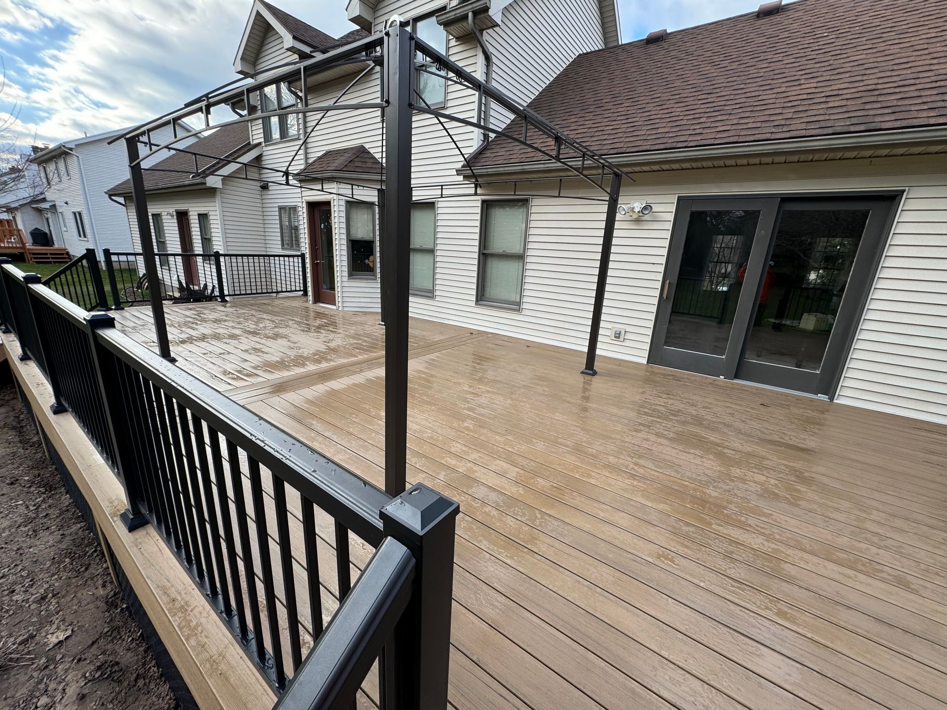 A wooden deck with a black railing in front of a house.