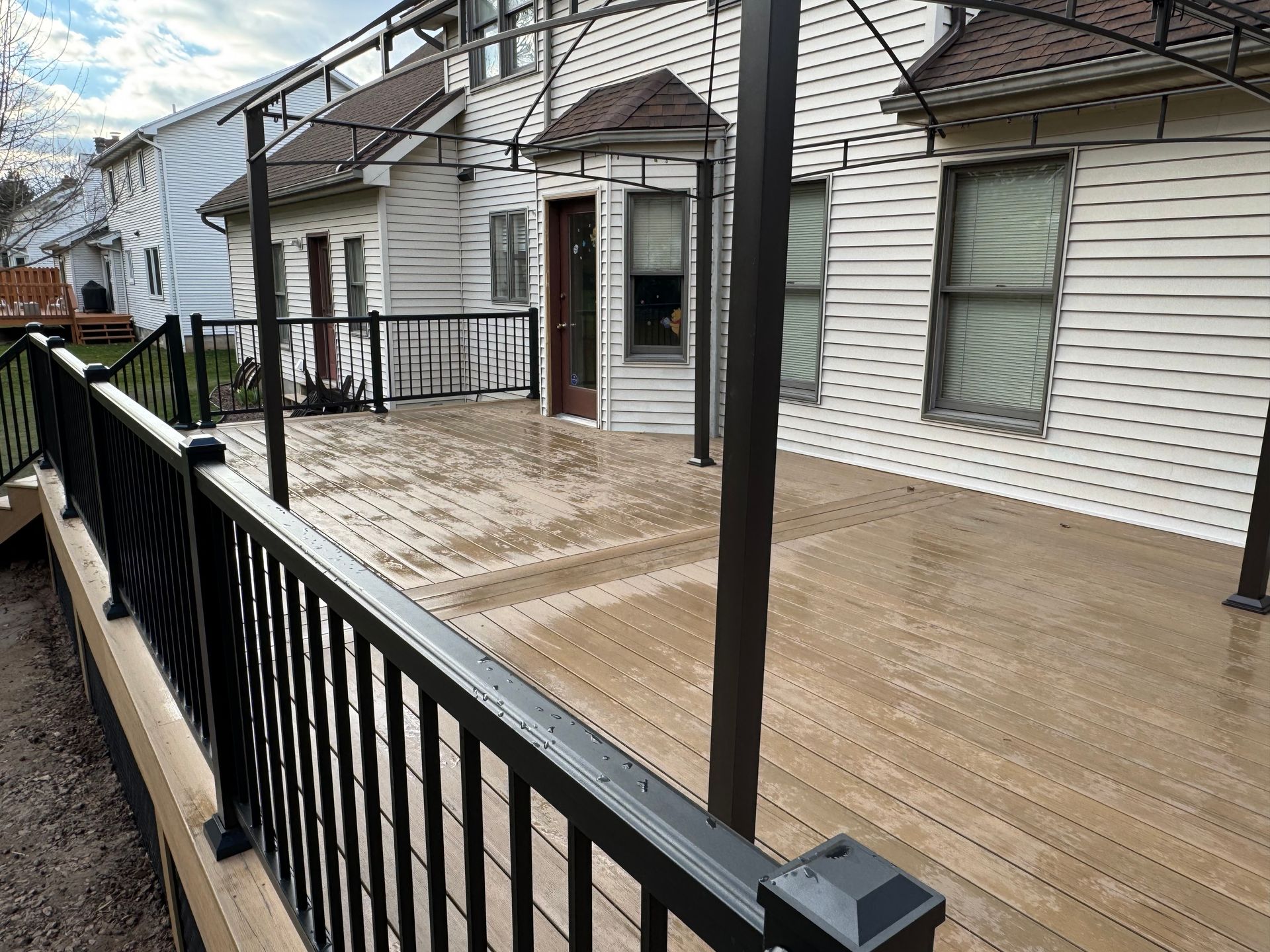 A large deck with a black railing in front of a white house.
